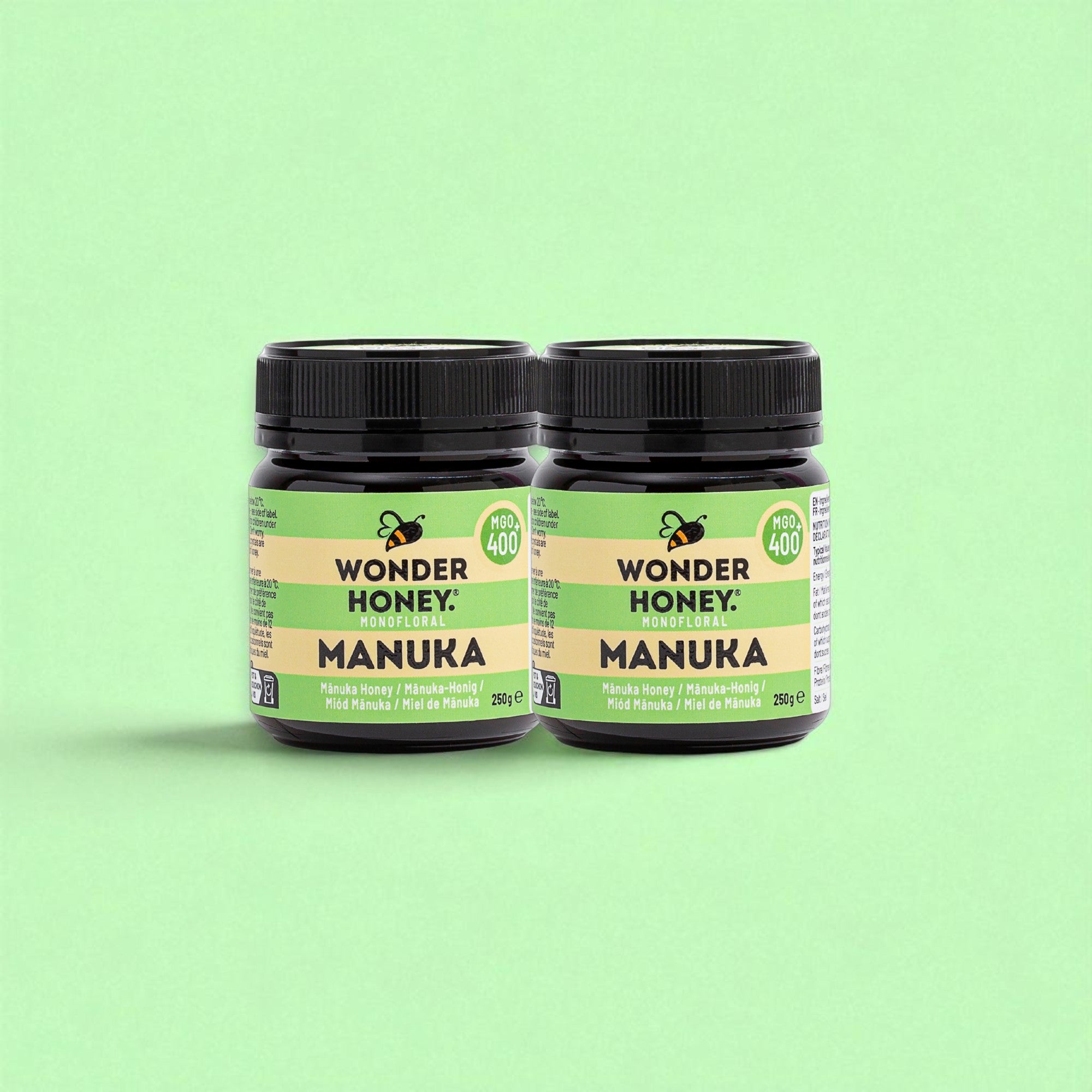 Two jars of Wonder Honey Manuka honey on a green background