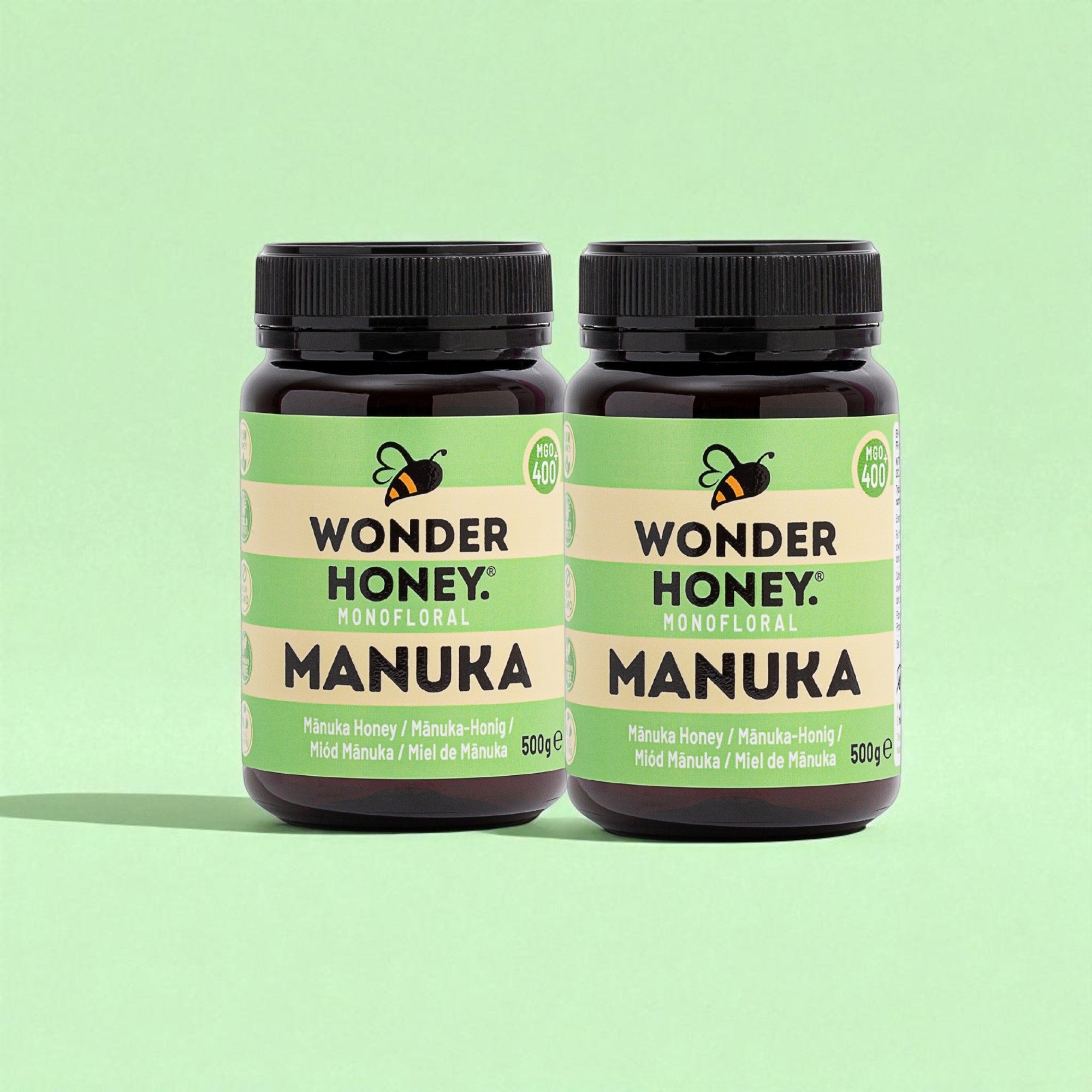 Two jars of Wonder Honey Manuka honey on a green background