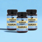 Three bottles of Wonder Honey Manuka honey on a blue background